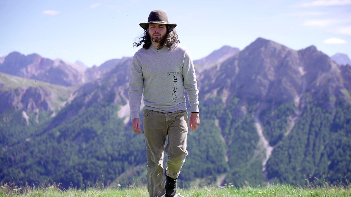 Benjamin Lechner geht mit Hut über einen Grat, hinter ihm die Bergkette.
