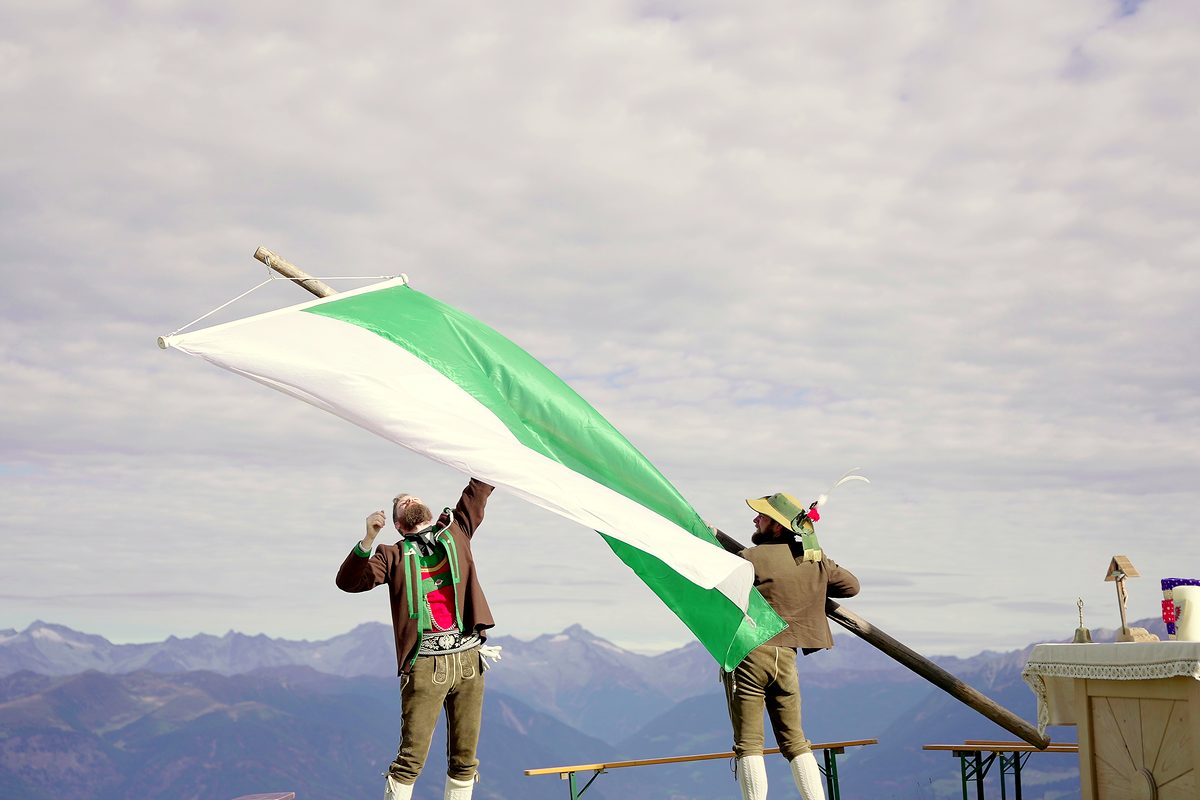 Ein Fahnenschwinger lässt die weiß grüne Fahne über dem Tal fliegen.
