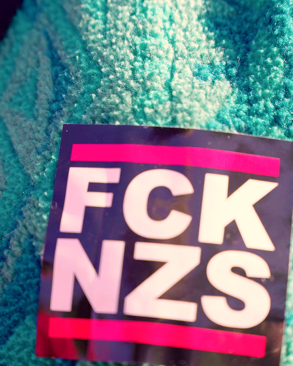 Ein pinker Aufnäher auf einer türkisen Fleecejacke, ganz nah.